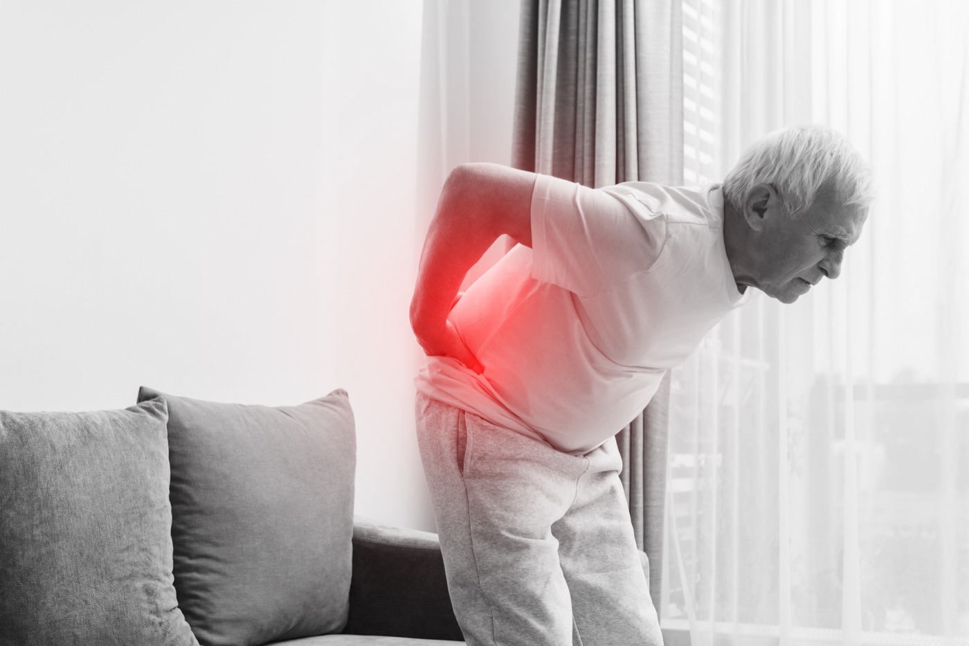 A person sitting and leaning forward with a pained expression, one hand at the lower back — the quiet experience of chronic low back and leg pain from a disc injury